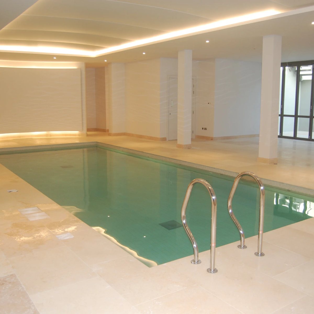 Contemporary basement pool with stone surround and coved lighting