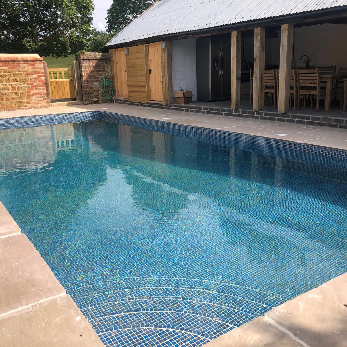 Outdoor pool finished in blue glass mosaic beside a barn